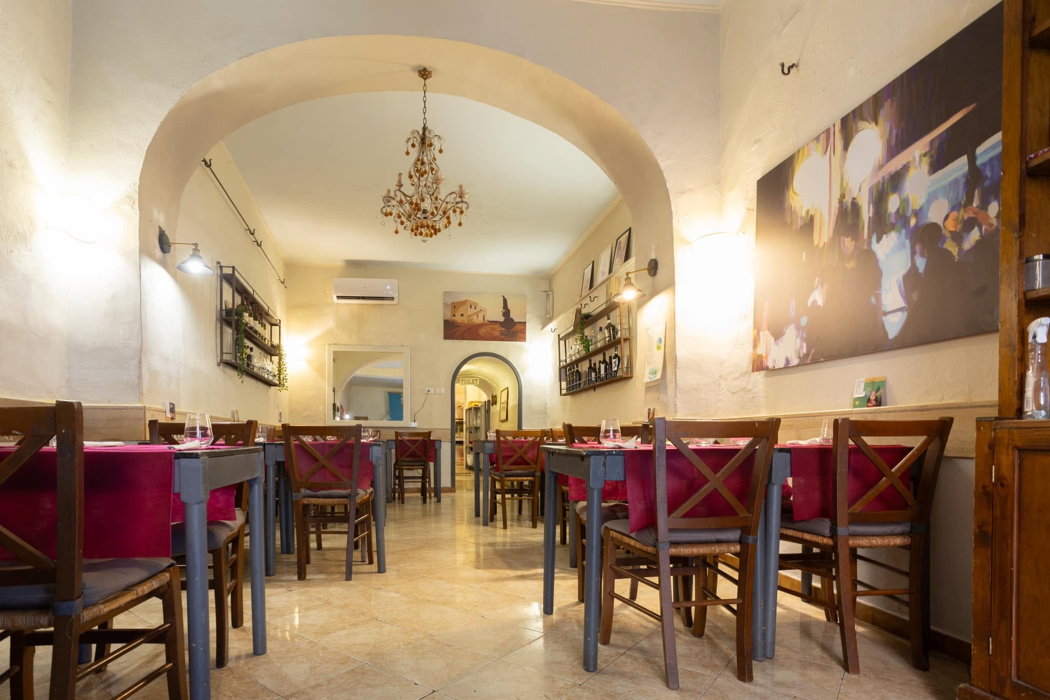 Sala di La Cicala e la Formica con arco, lampadario a gocce ambrate, tovaglie bordeaux e sedie in legno impagliate