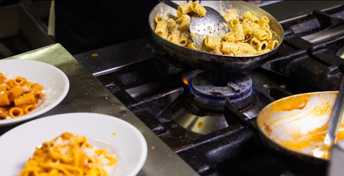 Rigatoni mantecati in padella sul fuoco a gas e piatti di pasta al pomodoro, cucina La Cicala e la Formica